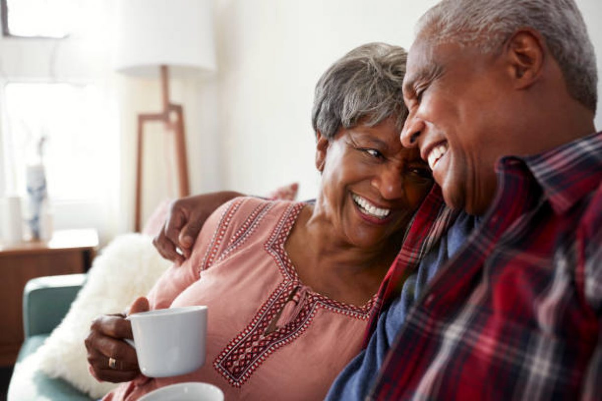 Loving Senior Couple Sitting On Sofa At Home Relaxing With Hot Drink